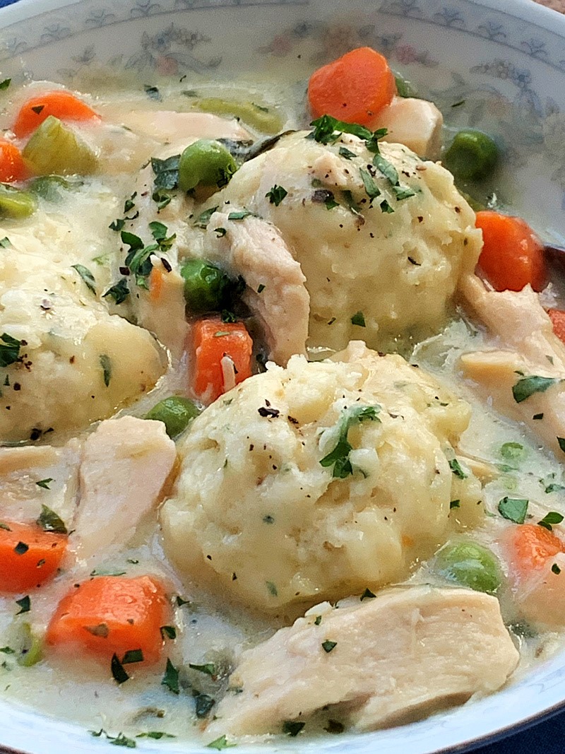 drop dumplings in a bowl of chicken and dumplings with carrots, garnished with parsley