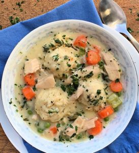white bowl filled with chicken and 3 dumplings garnished with parsley