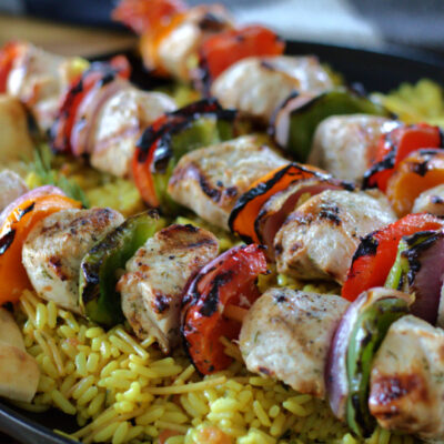 black plate with grilled mediterranean chicken kabobs over rice pilaf