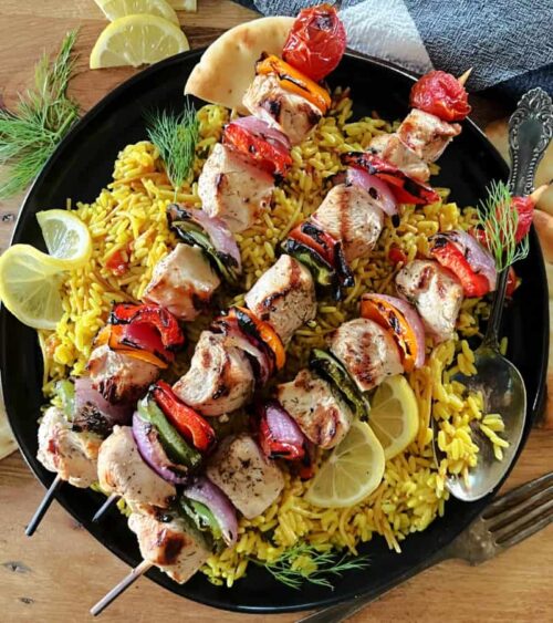 black plate with rice pilaf topped with Grilled Mediterranean Chicken Kabobs