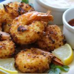 white plate with pile of golden coconut shrimp garnished with lemon