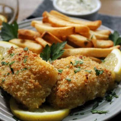 gray plate with crispy breaded cod, french fries and lemon wedges
