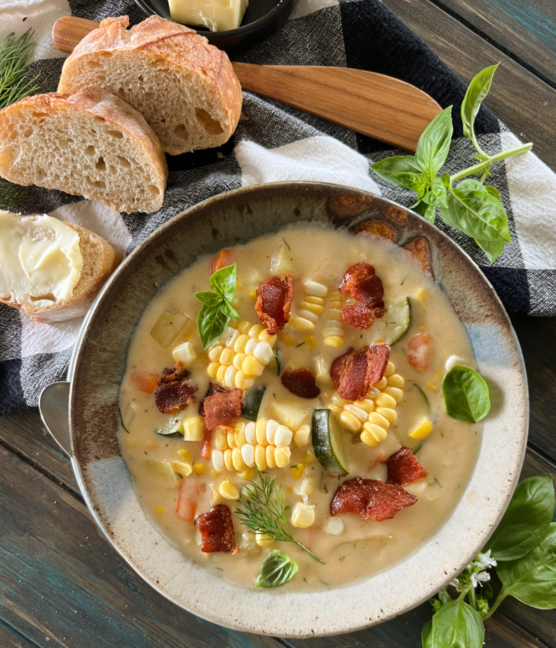 overhead view - bowl of cheesy corn chowder topped with crispy bacon, extra corn and fresh herbs