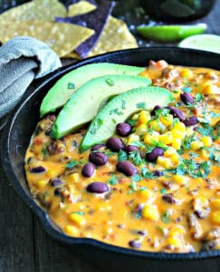 cast iron skillet with cowboy queso garnished with sliced avocado