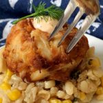 closeup of crab cake on bed of risotto pierced with seafood fork