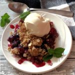 serving of mixed berry crisp topped with vanilla ice cream garnished with mint leaves