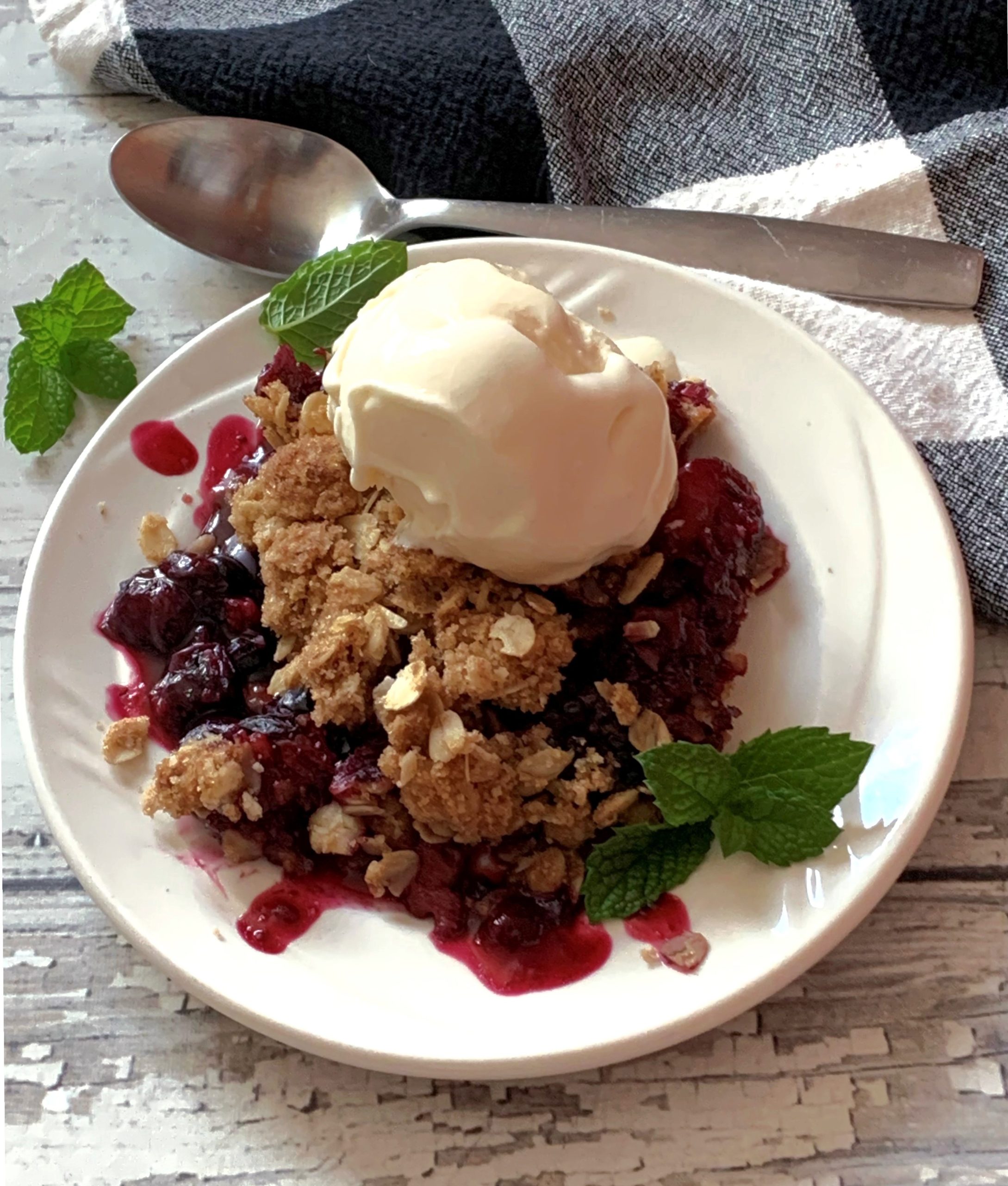 serving of mixed berry crisp topped with vanilla ice cream garnished with mint leaves