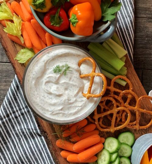overhead view bowl of dill dip surrounded by bright colored chopped vegetables