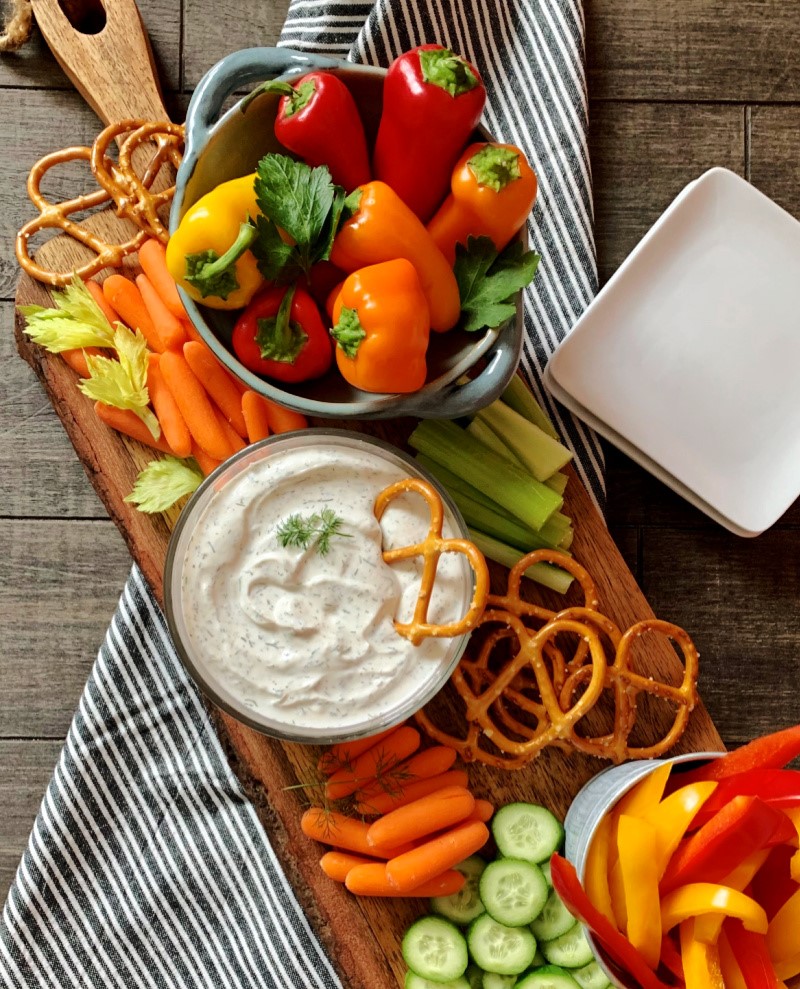 overhead view of clear bowl of dill dip with pretzels and bright colored vegetables
