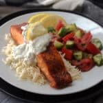 white plate with salmon with dill sauce, basmati rice and tomato cucumber salad