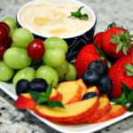 dip in a bowl shown with fresh strawberries, grapes, slices peaches and blueberries