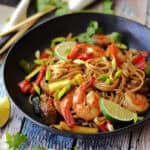 black bowl with drunken noodles garnished with lime wedge and cilantro