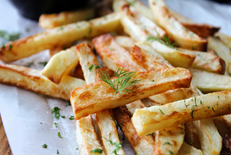 pile of air fryer french fries on parchment paper sprinkled with fresh herbs