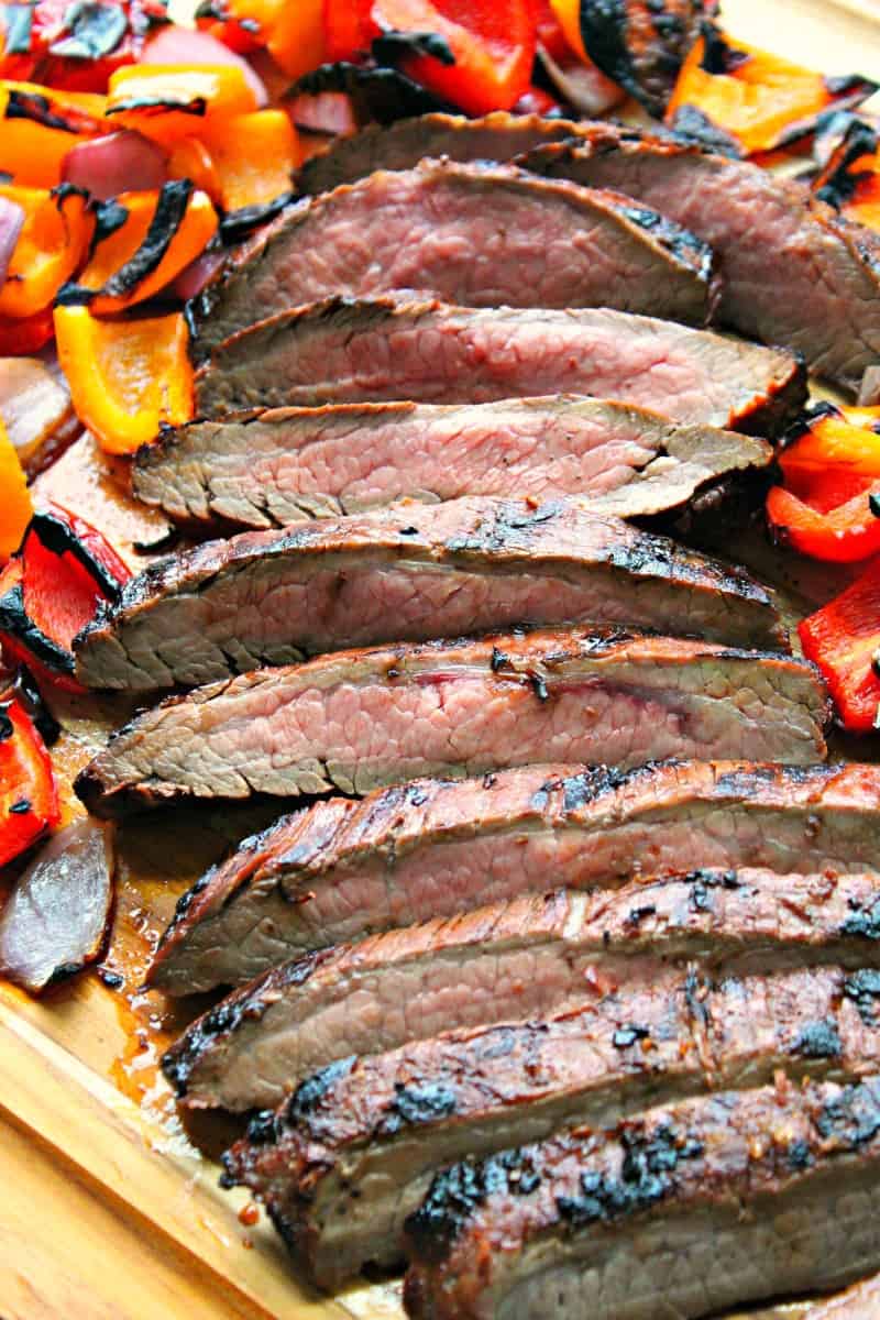 thin sliced grilled flank steak on a cutting board with bright colored grilled bell peppers