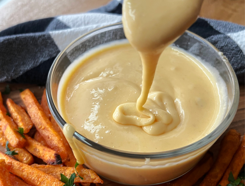clear bowl with flourless cheese sauce dripping from spoon