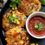 3 zucchini corn fritters on black plate with marinara for dipping