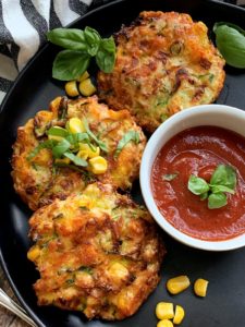 3 zucchini corn fritters on black plate with marinara for dipping