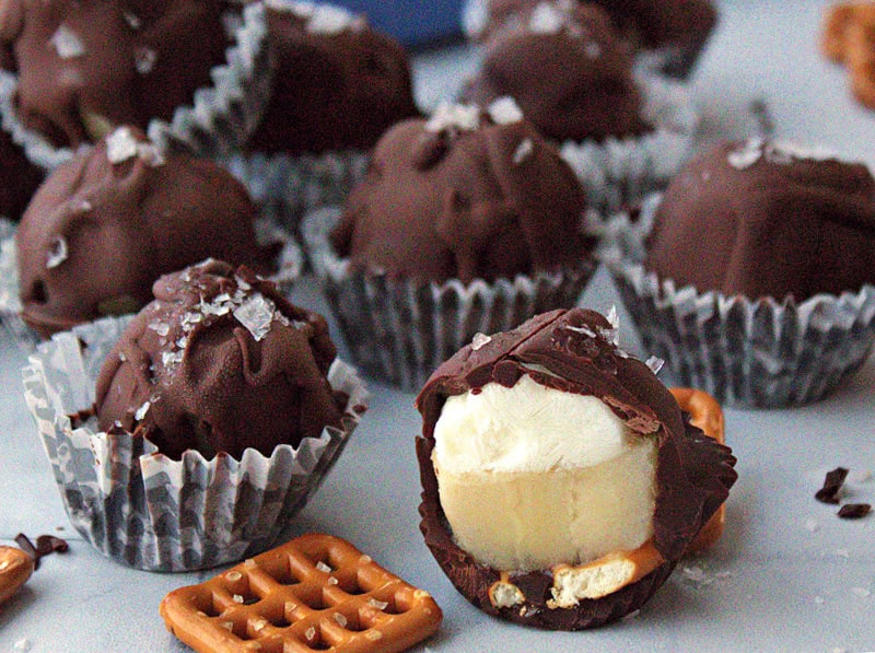 white plate with frozen chocolate banana yogurt bites surrounded by pretzels and chocolate shavings