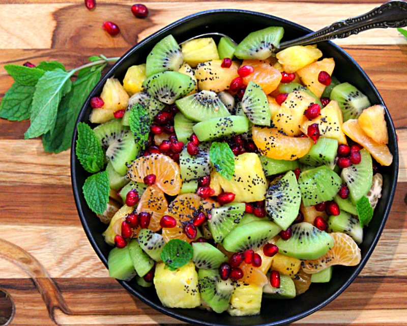black bowl filled with winter fruit salad of kiwi, pomegranate, mandarin and pineapple