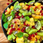 black bowl with winter fruit salad of pineapple, kiwi, mandarins and pomegranate