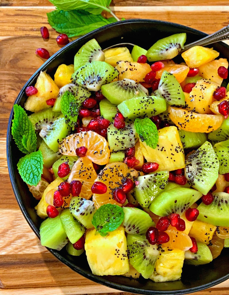 black bowl with winter fruit salad of pineapple, kiwi, mandarins and pomegranate