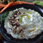 overhead view of black plate with garlic feta dip garnished with diced olives