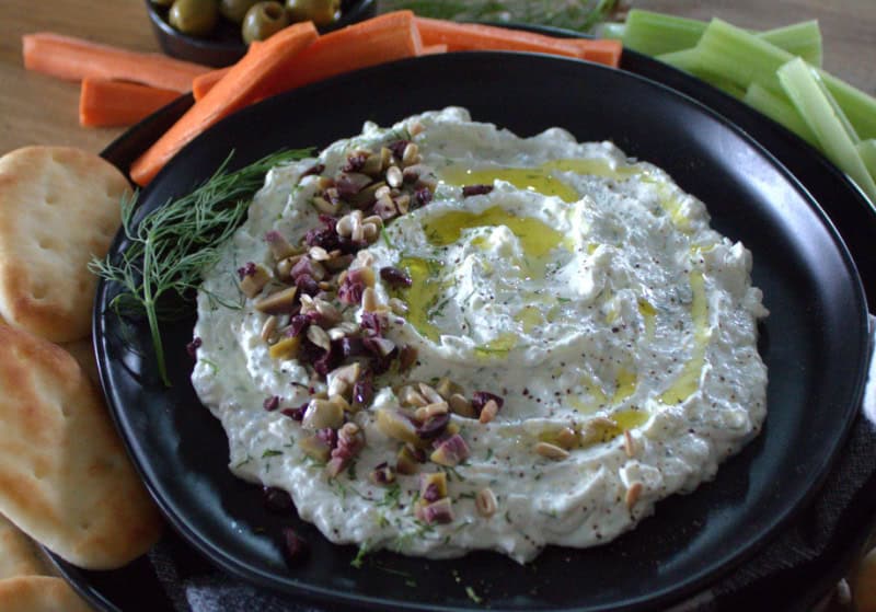 overhead view of black plate with garlic feta dip garnished with diced olives
