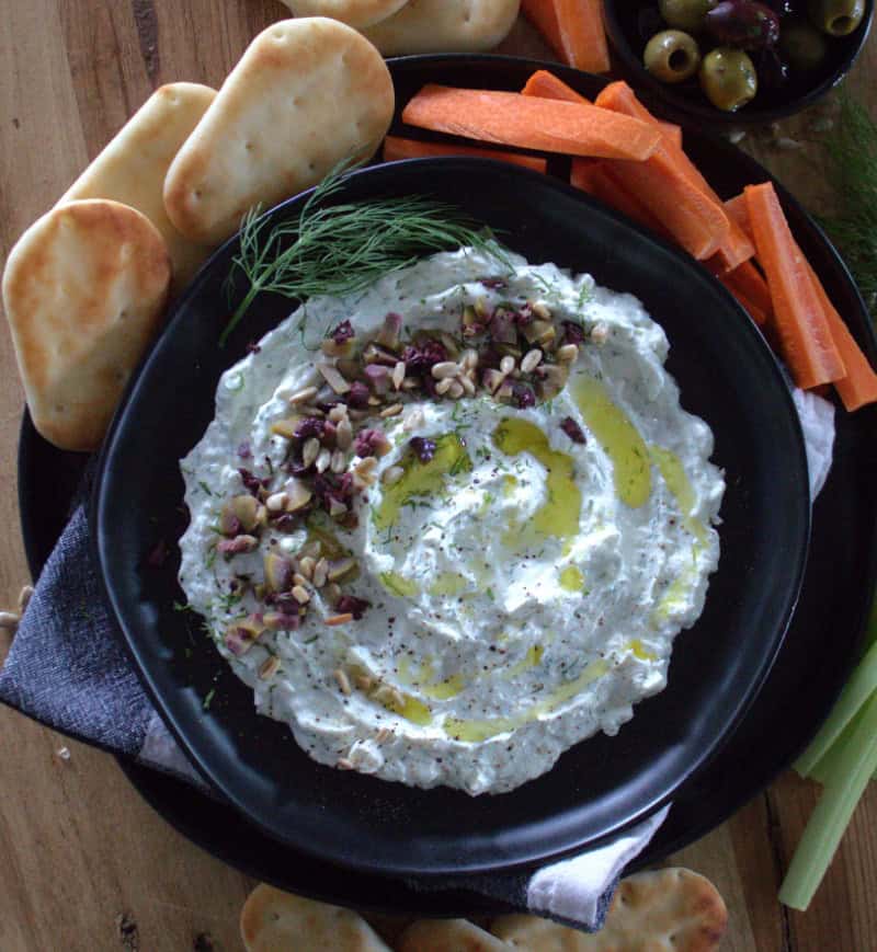 black plate with garlic feta dip garnished with chopped olives