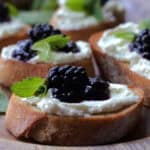 wooden tray with goat cheese blackberry crostini garnished with fresh mint
