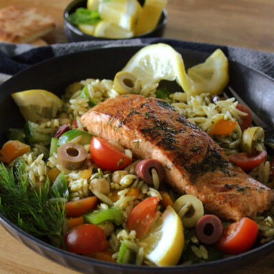 greek salmon on black plate with vegetable orzo