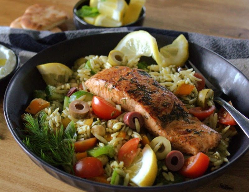 greek salmon on black plate with vegetable orzo