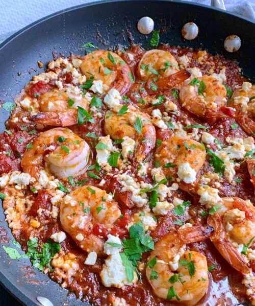 pan of green shrimp topped with feta cheese and chopped parsley