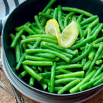 how to cook green beans - cooked beans shown in black bowl garnished with lemon slice