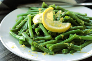 how to cook green beans - shown on white plate garnished with lemon slice.