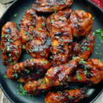 overhead view black plate with grilled spicy bbq chicken wings garnished with parsley