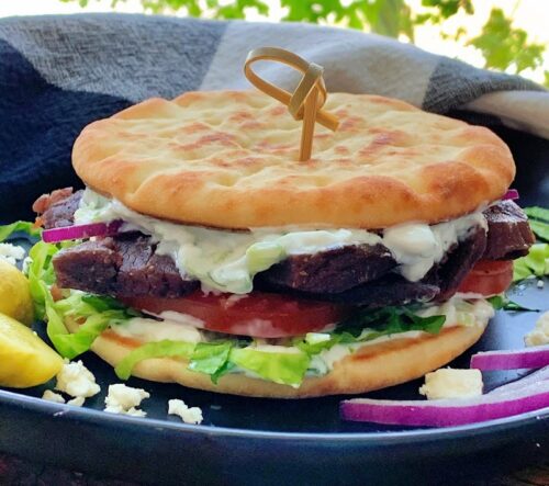Lamb gyro served sandwich style with top and bottom naans, yogurt sauce and tomato