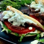 Two lamb gyros on black plate with yogurt sauce, sliced tomato and lettuce