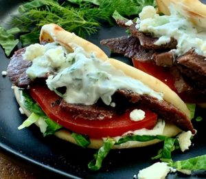 Two lamb gyros on black plate with yogurt sauce, sliced tomato and lettuce