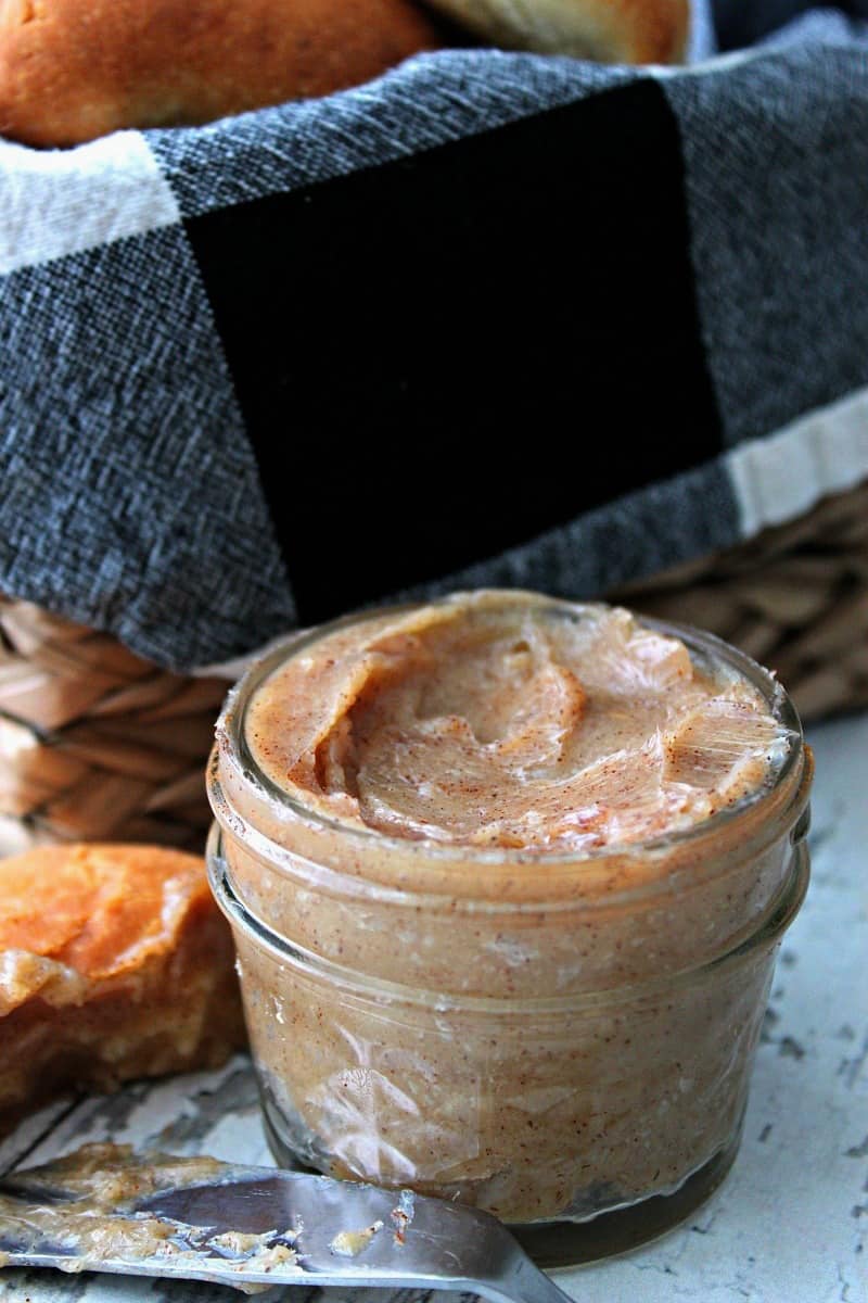 cinnamon honey butter in clear jar with basket of rolls in background