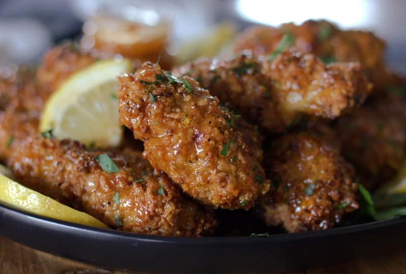 black plate with hot honey lemon pepper chicken and slices of lemon