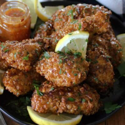 black plate with hot honey lemon pepper chicken tenders and slices of fresh lemon