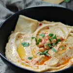 closeup - black bowl with hummus without tahini drizzled with olive oil and garnished with chickpeas