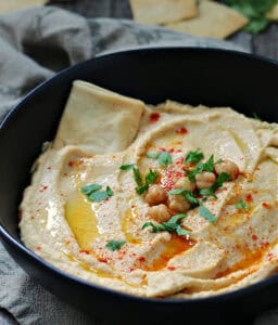 closeup - black bowl with hummus without tahini drizzled with olive oil and garnished with chickpeas