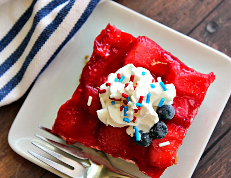 overhead view - white plate with square of strawberry pretzel jello topped with whipped cream and red and blue sprinkles