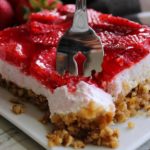 piece of strawberry pretzel jello on white plate with fork slicing into it