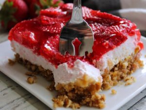 piece of strawberry pretzel jello on white plate with fork slicing into it