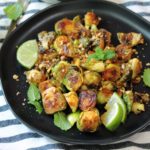 black plate with caramelized glazed brussels sprouts halves garnished with crushed peanuts and lime wedge