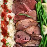 sliced roast of lamb with rice and green beans on white platter