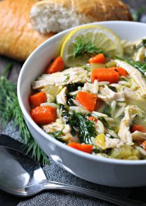 lemon chicken orzo soup ~ closeup of soup loaded with shredded chicken, carrots, orzo, fresh dill sprigs and a slice of lemon.