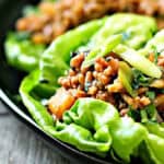 black plate with chicken lettuce wraps garnished with green onions